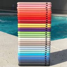 a stack of colored notebooks sitting next to a pool with water in the background