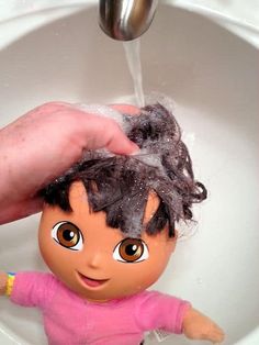 a doll being washed in a sink by someone's hand with water coming out of the faucet