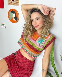 a beautiful young woman in a colorful top and skirt leaning against a wall with her hand on her head