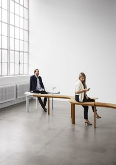 two people sitting on benches in an empty room with one woman using her cell phone