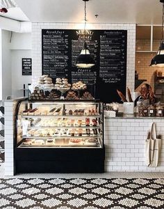 the interior of a bakery with black and white tiles on the floor, chalkboard menus hanging from the ceiling