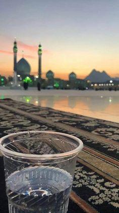 a plastic cup sitting on top of a rug next to a body of water at sunset