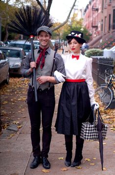 a man and woman dressed in costumes standing next to each other on a sidewalk with umbrellas