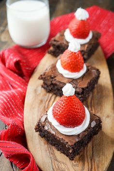 chocolate brownies with strawberries and whipped cream on top are sitting on a wooden platter