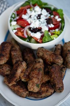 a white plate topped with meat patties next to a salad