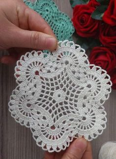 two hands are holding crocheted doily next to red roses