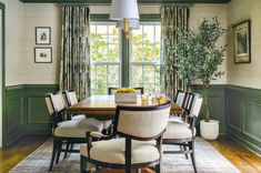 a dinning room with green walls and wood flooring, along with a dining table surrounded by beige upholstered chairs