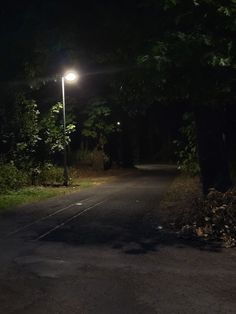 an empty road at night with a street light on the side and trees in the background