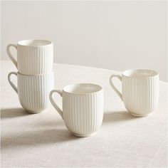 three white mugs sitting on top of a table next to each other with handles