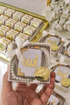 a person holding up a small box with gold foil lettering on it and some other boxes in the background