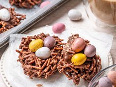 some kind of bird's nest cookies on a plate with candy eggs and pretzels