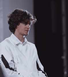 a young man sitting in a chair with his hand on his hip and looking off to the side