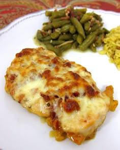 a white plate topped with meat covered in cheese and veggies next to green beans