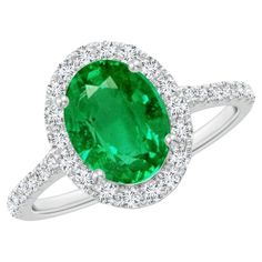 an oval shaped emerald and diamond ring with halos on the sides, set in 18k white gold