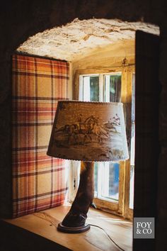 a lamp sitting on top of a wooden table in front of a plaid wallpapered window