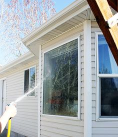 a man is spraying water on a house's windows with a yellow sprayer