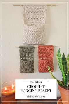 three crochet hanging baskets on a wall next to a potted plant and candle