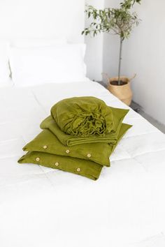 two folded green blankets on top of a white bed with a potted plant in the corner