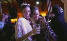 two women are hugging each other at a party with one holding a glass in her hand