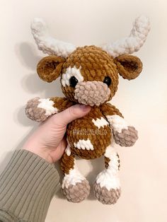 a hand holding a brown and white crocheted stuffed animal with horns on it's head