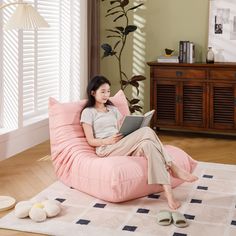 a woman sitting on a pink bean bag chair reading a book in her living room