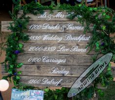 a wooden sign that has some writing on it with flowers around it and two surfboards next to it