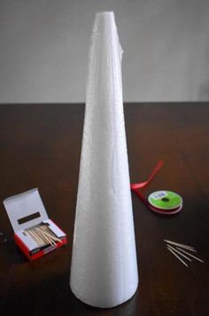 a white cone shaped object sitting on top of a wooden table next to scissors and thread