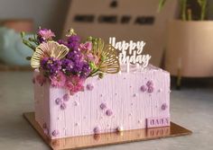 a pink birthday cake with flowers on it and a happy birthday sign in the middle