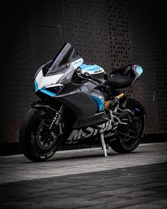 a blue and white motorcycle parked in front of a metal wall with perforated panels