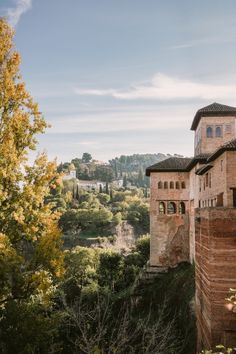 an old building on the side of a hill with trees around it and hills in the background