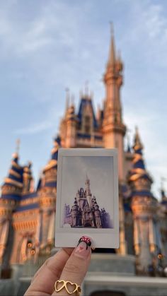 a hand holding up a small photo in front of a building with a castle on it