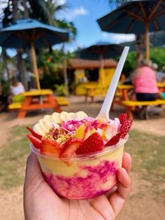 a person holding up a bowl of food with fruit in it and an umbrella behind them