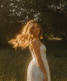 a woman in a white dress is standing in the grass with her hair blowing in the wind