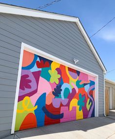 a garage door painted with an abstract painting on it's side and attached to the side of a house