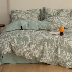 a bed with green and white comforter on top of it next to a night stand