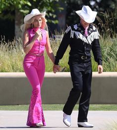 a man in a cowboy hat and pink outfit walking next to a woman in a pink jumpsuit