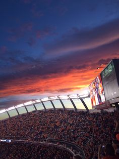 a stadium filled with lots of people watching a football game at sunset or sunrise time