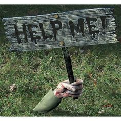 a hand holding a sign that says help me on it in front of some grass