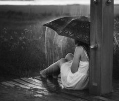 a woman sitting under an umbrella in the rain