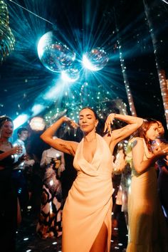 a woman in a white dress dancing at a party with people around her and disco lights