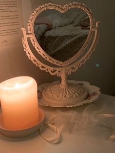 a lit candle sitting on top of a white table next to a mirror with a heart shaped frame