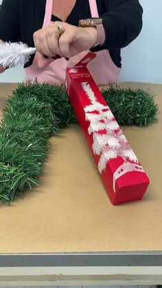 a woman in an apron is decorating a red box with white feathers and grass