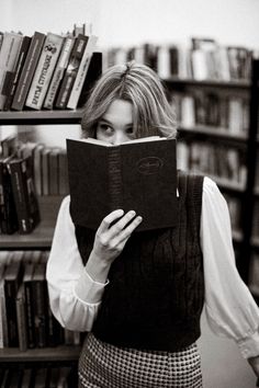 a woman standing in front of a bookshelf holding a book up to her face