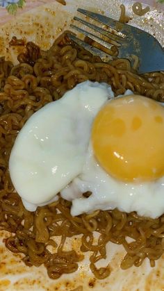 an egg is on top of noodles in a plate with a fork and knife next to it