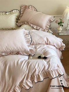 a bed with pink comforters and pillows on top of it, next to a night stand