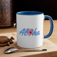 a blue and white coffee mug with the word aloha on it next to a cookie