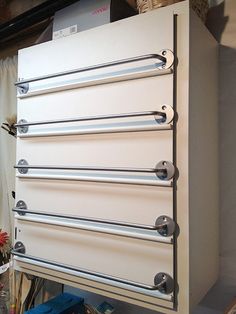 a white cabinet with four metal handles on the top and bottom, sitting in a room