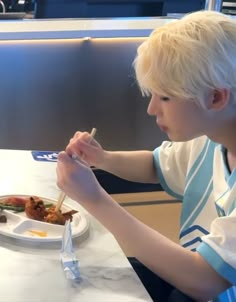 a young boy sitting at a table eating food with chopsticks in his hand