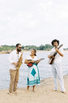 two men and a woman playing instruments on the beach