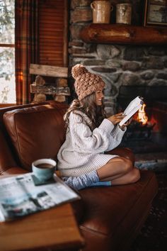 a woman sitting on a couch in front of a fireplace holding a book and smiling